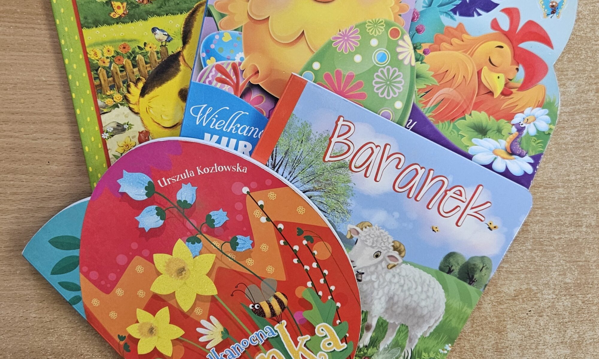 Zdjęcie przedstawia 5 kolorowych książek dziecięcych o Wielkanocy. Książki ułożone są na drewnianej powierzchni.