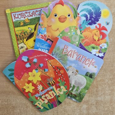Zdjęcie przedstawia 5 kolorowych książek dziecięcych o Wielkanocy. Książki ułożone są na drewnianej powierzchni.