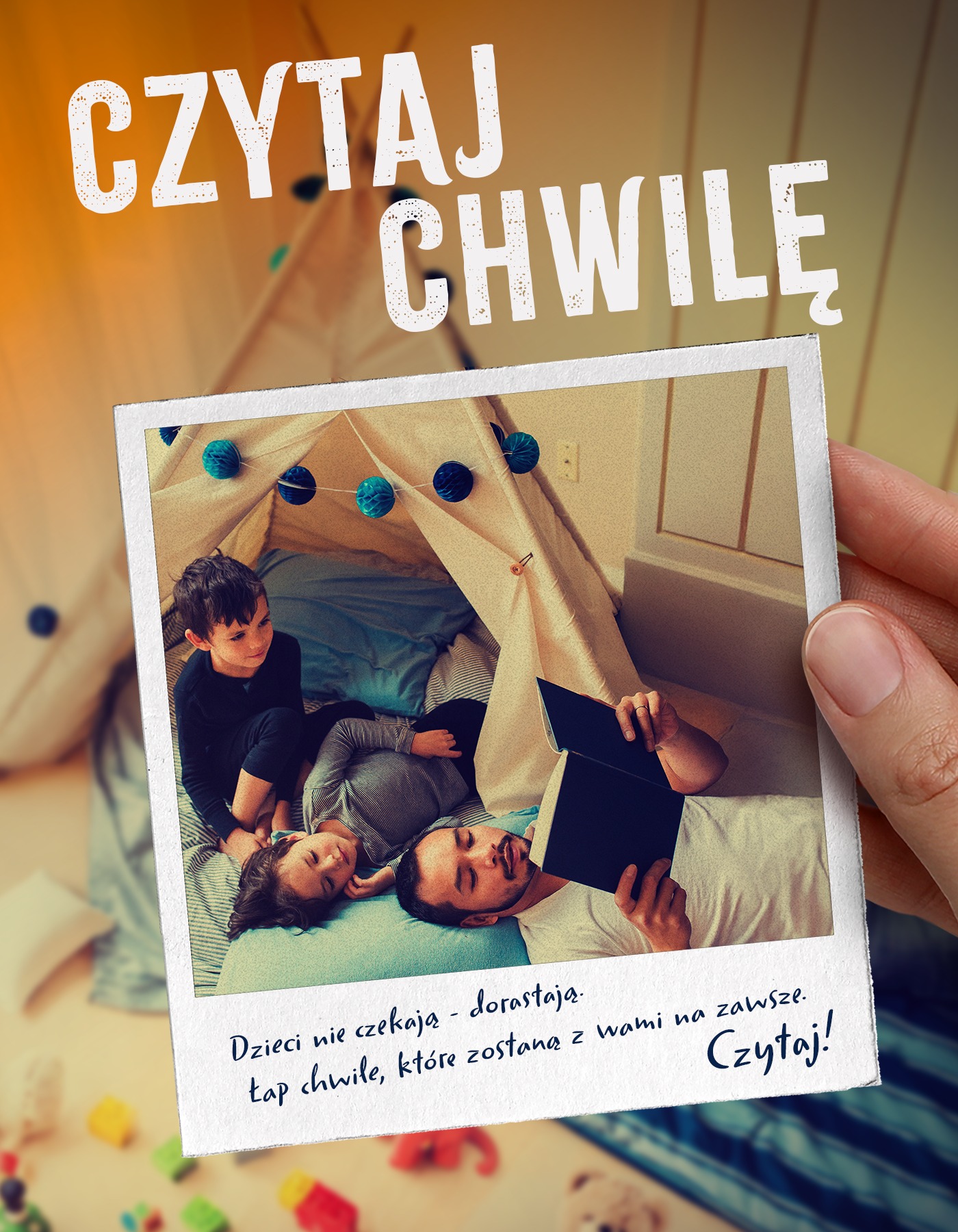 Plakat przedstawia trzymają w dłoni fotografię, na której znajdują się trzy osoby: dorosły mężczyzna trzymający książkę oraz dwoje dzieci. Pod zdjęciem jest podpis: Dzieci nie czekają - dorastają. Łap chwile, które zostaną z wami na zawsze. Czytaj!. Nad fotografią jest napis: Czytaj chwilę.